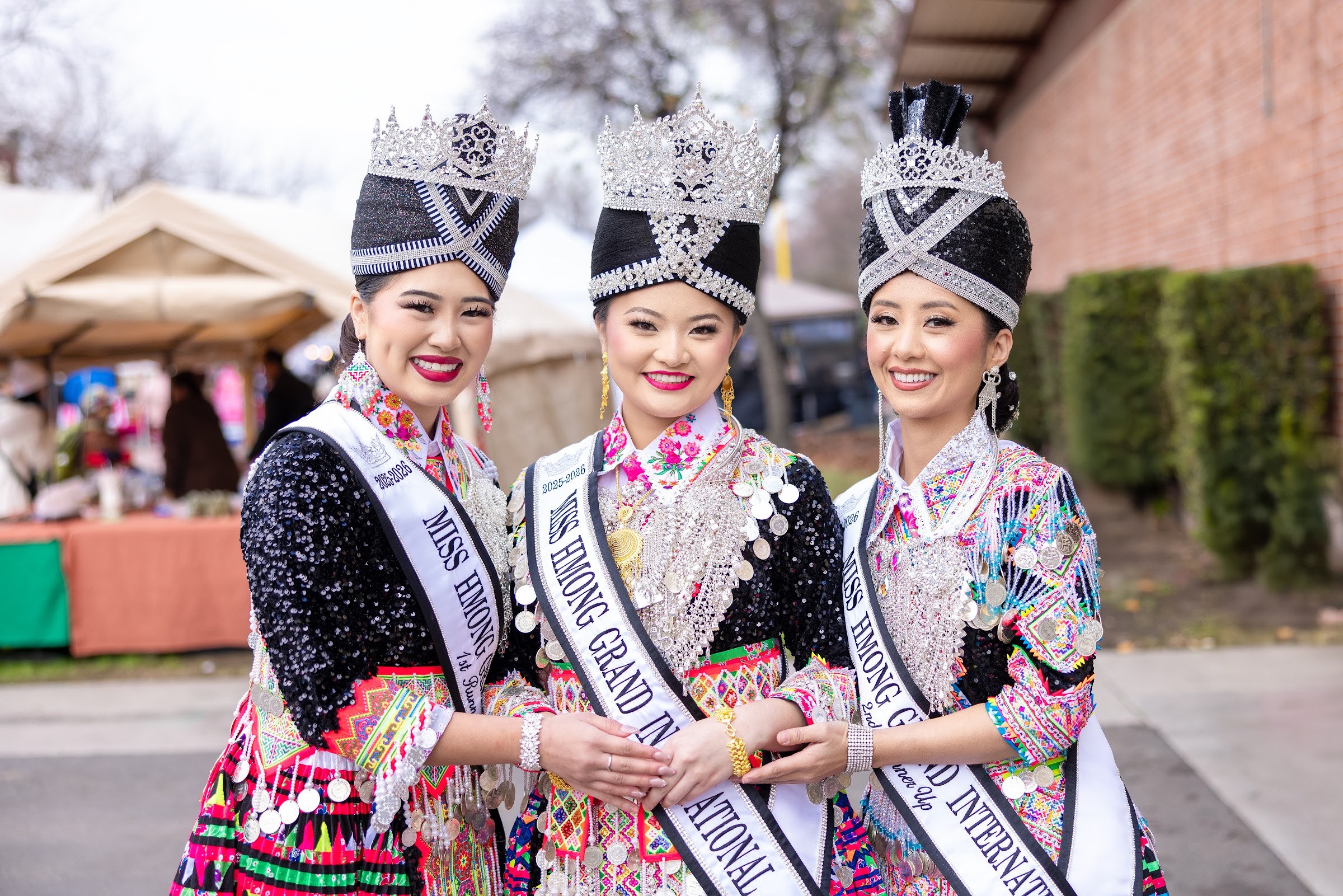Three Miss Hmong Grand International titleholders in full regalia and silver crowns at the Big Fresno Hmong New Year.