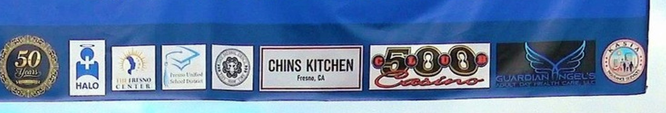Sponsor logos on the welcome arch banner at the 2026 Big Fresno Hmong New Year: HALO Hospice, The Fresno Center, Fresno Unified School District, Chin's Kitchen, 500 Club Casino, Guardian Angel's and others.